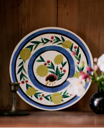 Decorative ceramic plate with blue rim and hand-painted floral design featuring yellow flowers, green leaves, and red berries on white background.