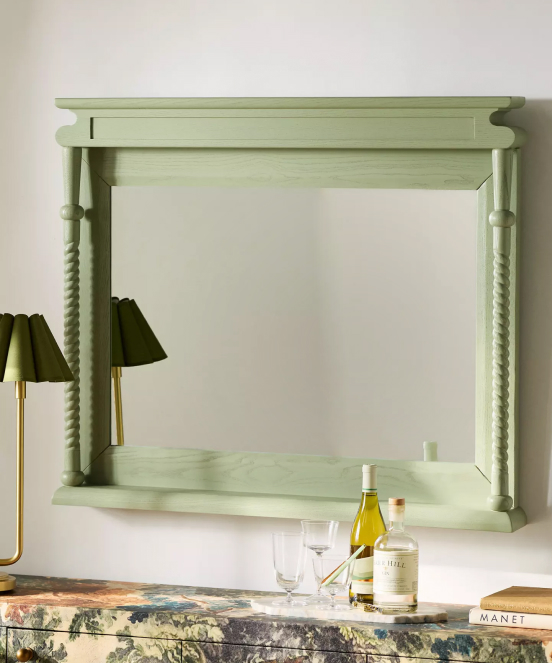 Sage green wooden mirror with decorative turned columns and shelf, mounted on white wall above marble surface
