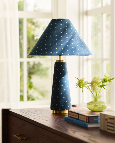 Blue table lamp with white polka dot pattern on shade and base, displayed on wooden surface with books and green vase nearby.