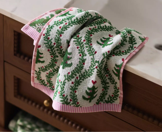 White towel with green embroidered fern leaves and pink berries, pink striped border, draped on wooden furniture.