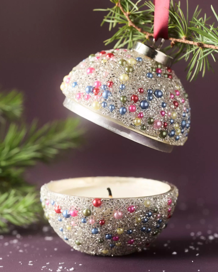 White ornament decorated with colorful beads and glitter, split in half with top hanging from tree branch and bottom as candle holder.