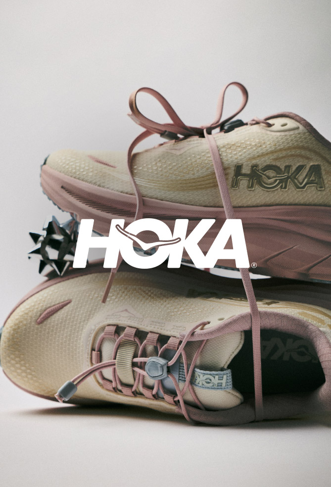 Pair of beige and pink HOKA running shoes with laces tied together, displayed with white HOKA logo overlay on neutral background.