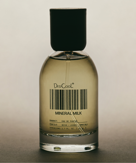 Perfume bottle with golden liquid and black cap labeled DedCool MINERAL MILK with barcode on beige background