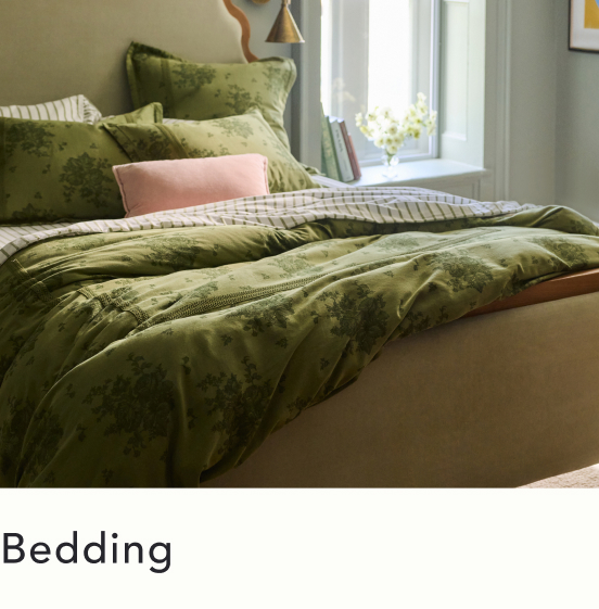 Bed with olive green floral duvet and pillows, pink accent pillow, beige base, window with flowers in background. Text: Bedding