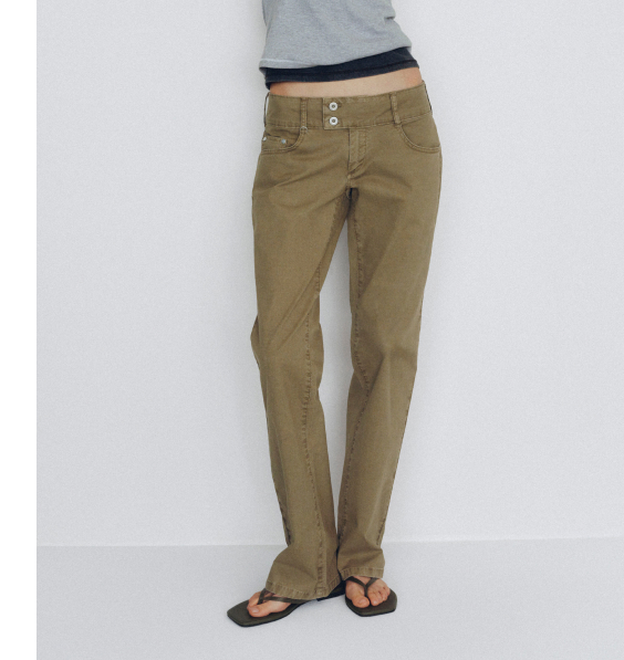 Woman wearing olive green pants with two-button waist, gray top, and brown sandals on white background.