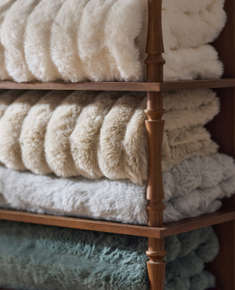Neatly rolled white and cream towels stacked on wooden bamboo shelves with a teal towel on the bottom shelf.