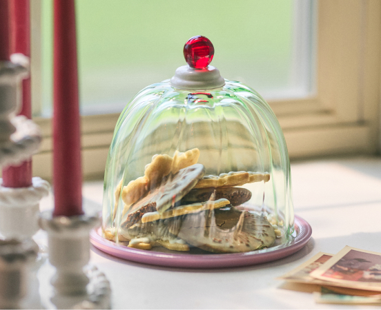 Glass dome with red knob on pink plate displaying stacked cookies, with text "Kitchen & Dining" below
