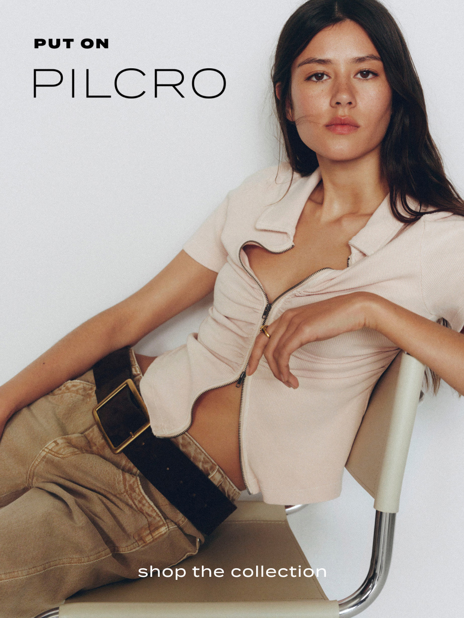 Woman in beige zip-up top and tan pants sitting on white chair. Text reads "PUT ON PILCRO" and "shop the collection"