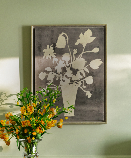 Framed gray floral silhouette artwork on sage green wall with vase of orange roses in foreground