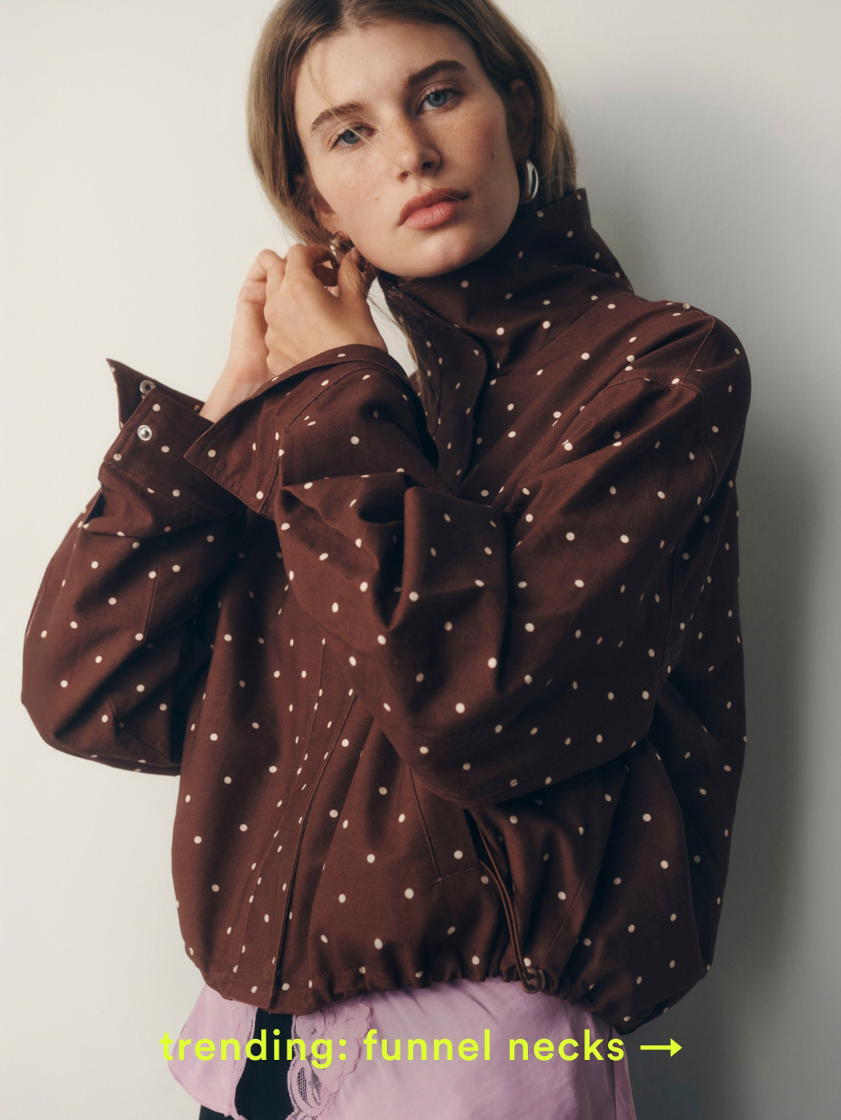 Woman wearing brown polka dot jacket with funnel neck and pink tulle skirt. Text reads "trending: funnel necks →"
