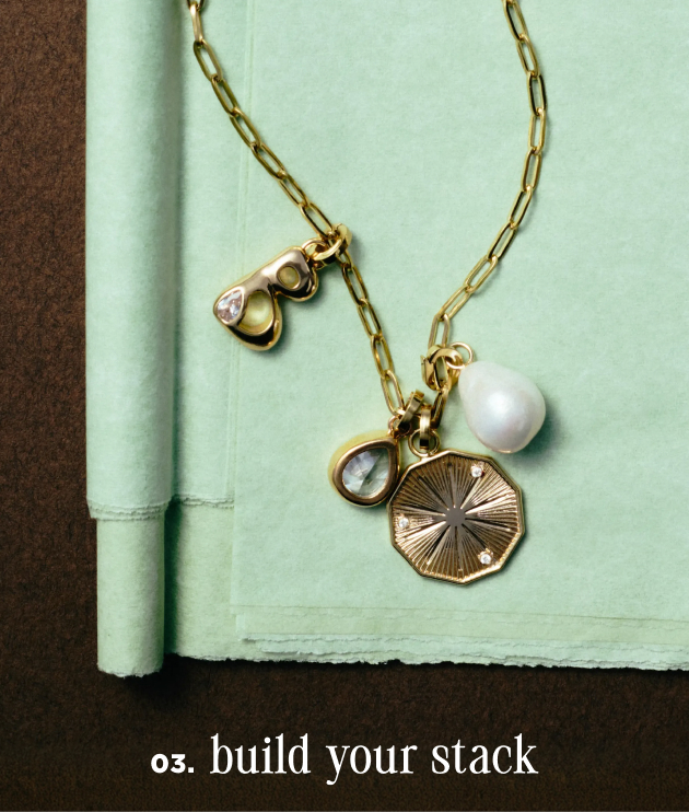 Gold chain necklace with pearl and charm pendants on mint green notebook with text "03. build your stack"