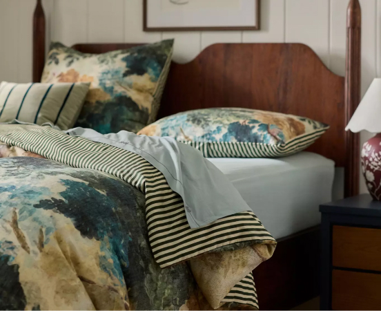 Unmade bed with wooden headboard featuring teal and beige floral bedding with black and white striped accent blanket.