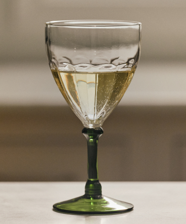 Clear glass goblet with green stem filled halfway with white wine against a neutral beige background.