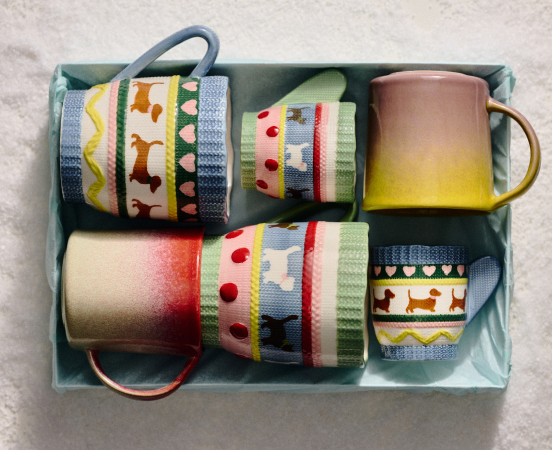 Four decorative mugs with colorful patterns including dogs, hearts, and geometric designs, arranged in a light blue gift box.