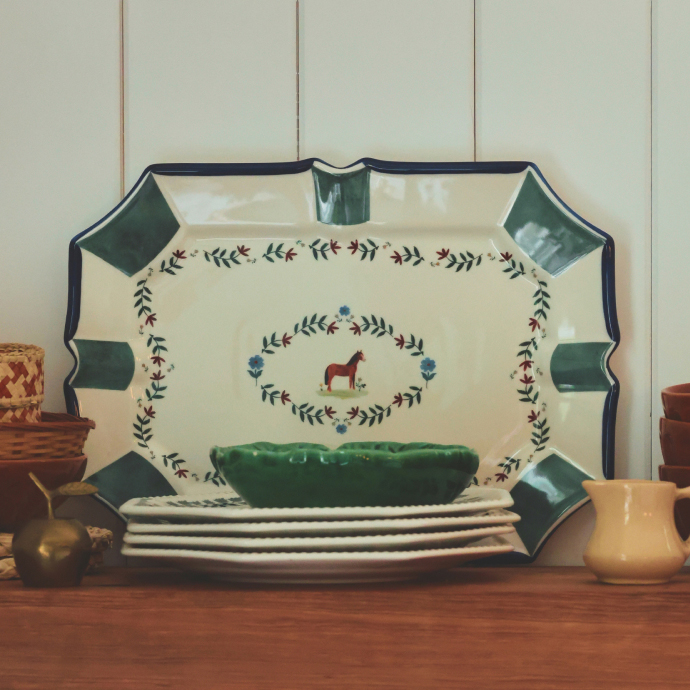 Decorative ceramic platter with green corners, cream center, floral vine border, and red horse motif displayed with stacked plates