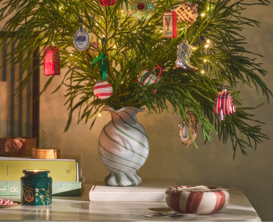 Decorated evergreen branches in a marbled vase with colorful ornaments, lights, and wrapped gifts on a white surface
