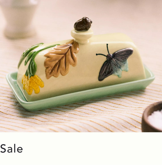 Ceramic butter dish with green base and cream lid decorated with butterfly, leaves, and yellow flower, with Sale text below