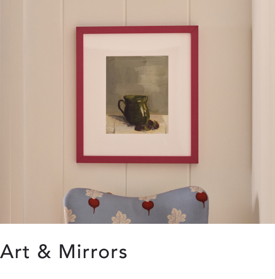 Framed still life painting of a green pitcher in red frame above blue floral pillow with text Art & Mirrors below