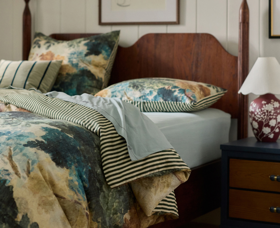 Bed with floral teal and beige duvet, striped trim, wooden headboard, white pillows, and nightstand with decorative vase.