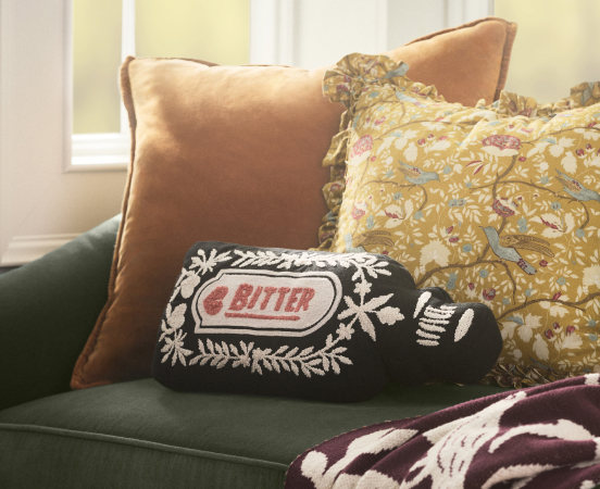 Decorative throw pillows on a green sofa, including a black pillow with white floral design and "BITTER" text in red oval.