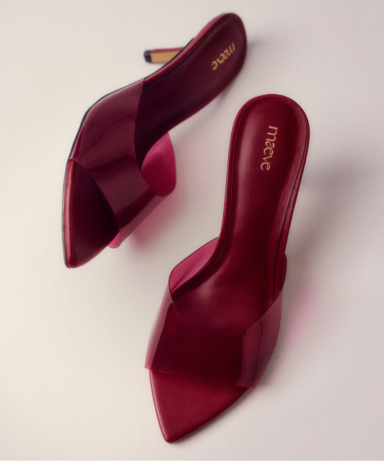 Pair of burgundy satin mule heels with pointed toes and crisscross straps, branded "mecie" on insole, on beige background.