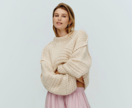 Woman wearing cream chunky knit sweater and pink skirt against light blue background