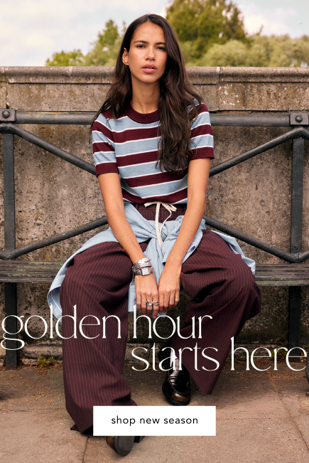 Woman in burgundy and white striped shirt and wide-leg pants sitting outdoors. Text reads "golden hour starts here shop new season"