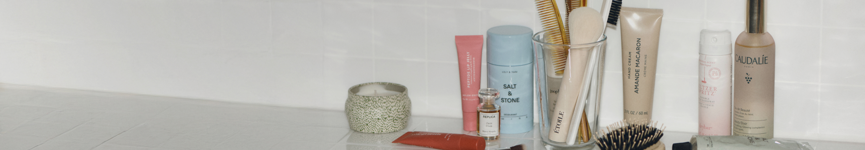 Bathroom counter with beauty products including Salt & Stone deodorant, Caudalie spray, hairbrushes in holder, and skincare items.