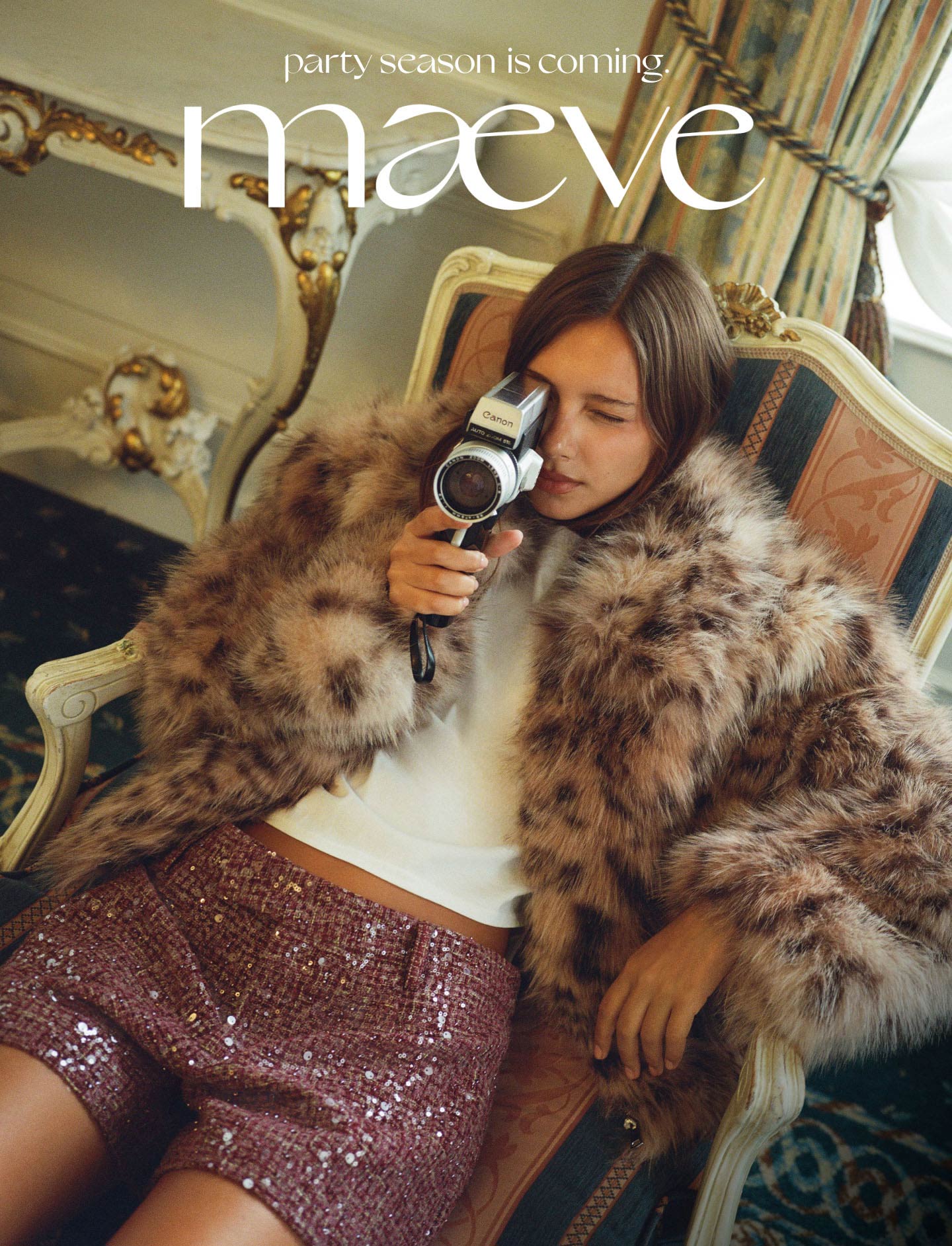 Woman in fur coat and pink sequin skirt holding vintage camera on ornate chair. Text reads party season is coming maeve.