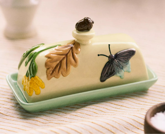 Ceramic butter dish with decorative lid featuring sculpted butterfly, leaves, and flowers on a green base plate.