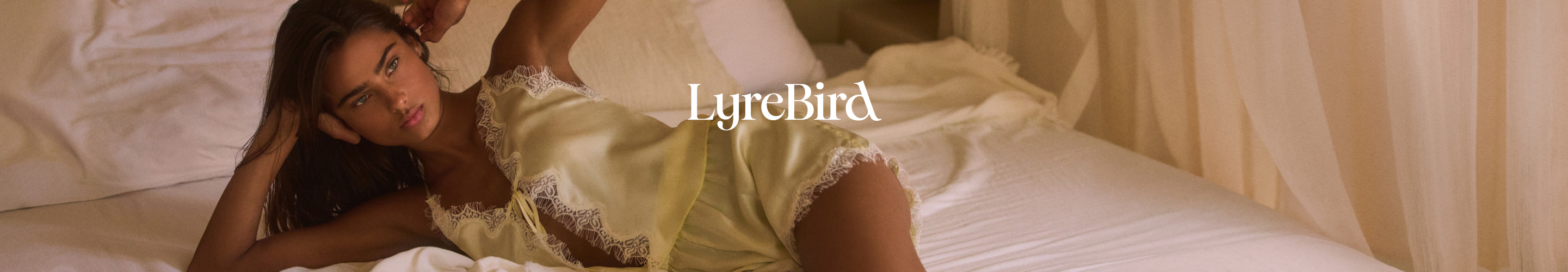Woman reclining on bed wearing yellow lace-trimmed lingerie with LyreBird text overlay in white