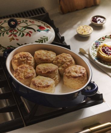 Golden-brown stuffed dumplings cooking in a black pot on a stovetop, with decorative floral pot holder and garnished plate nearby.