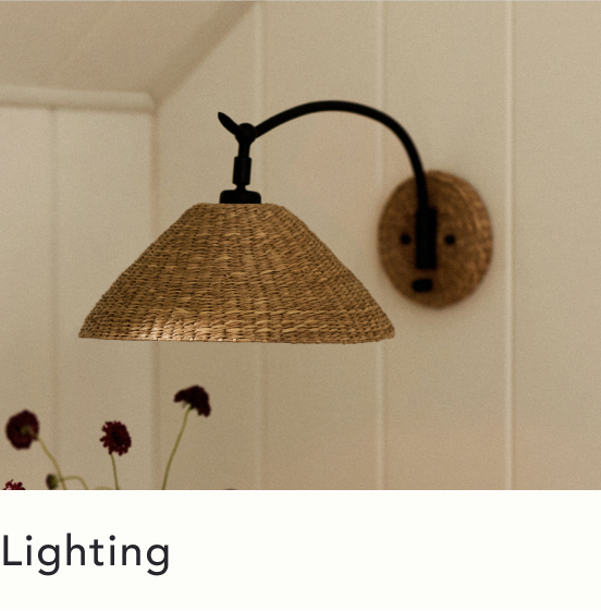 Wall-mounted lamp with woven rattan conical shade and black metal arm against white paneled wall with text Lighting below