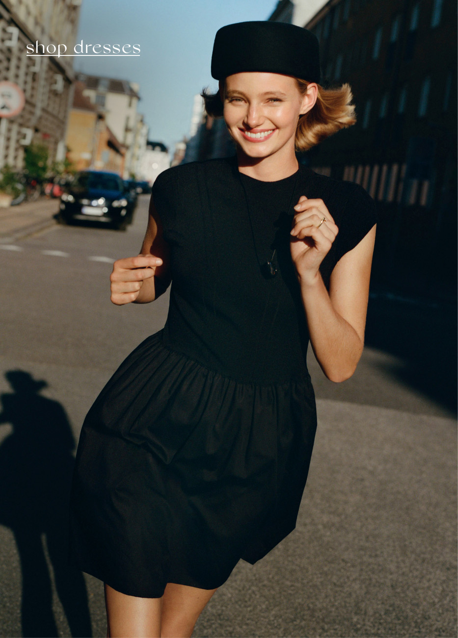 Smiling woman in black dress and beret on city street with text shop dresses in upper left corner