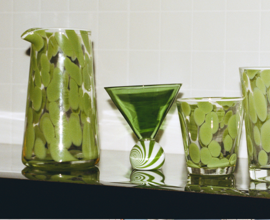 Green glass drinkware collection including a pitcher, martini glass, and tumblers with decorative white patterns