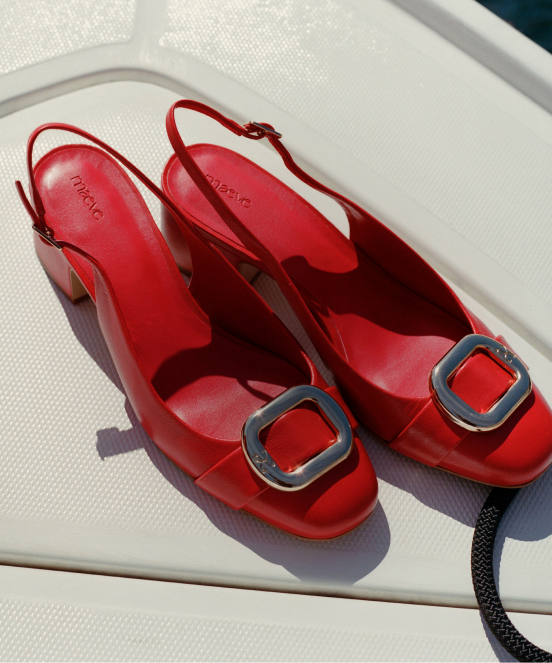 Red jelly slingback sandals with silver square buckle detail on white outdoor chair in sunlight