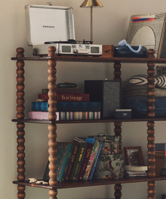 Wooden shelving unit with spindle legs displaying a Crosley record player, books, vinyl records, and decorative items.