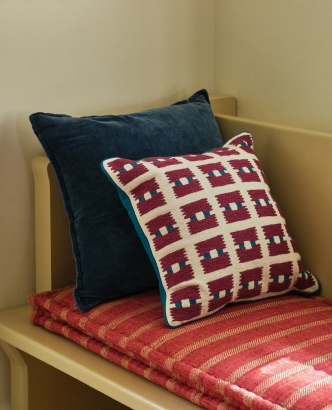 Two decorative pillows on a wooden bench: a navy blue pillow and a cream pillow with red and navy geometric pattern.