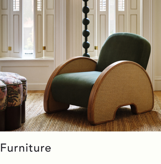 Green velvet armchair with curved rattan sides on a jute rug, with white shuttered windows and floral ottoman in background