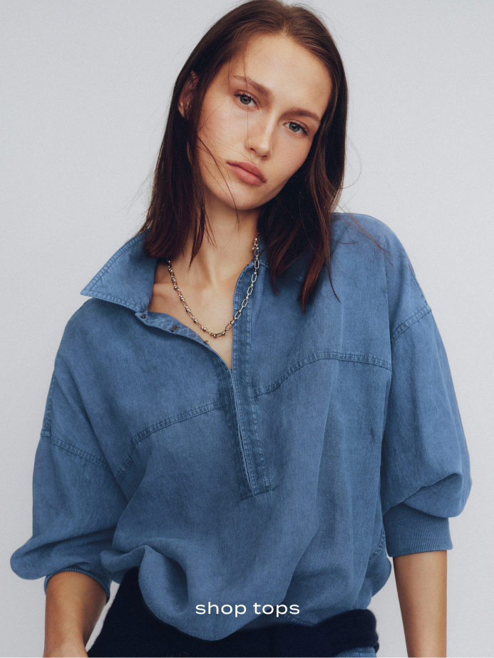 Woman wearing oversized blue denim shirt with silver chain necklace against light background with text "shop tops"