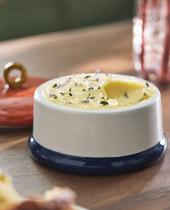 White bowl with melted butter topped with herbs on a wooden board with garlic cloves nearby