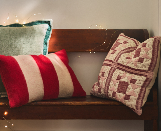 Decorative pillows on a wooden bench: red and white striped pillow, geometric patterned pillow, and teal-trimmed pillow.
