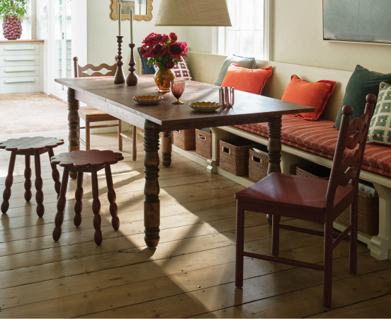 Cozy dining area with dark wood table, built-in bench seating with orange cushions, wooden stools, and natural light.