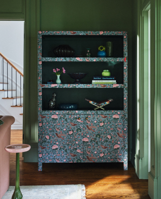 Decorative cabinet with floral pattern trim and dark shelves displaying colorful items, set in green-walled room.