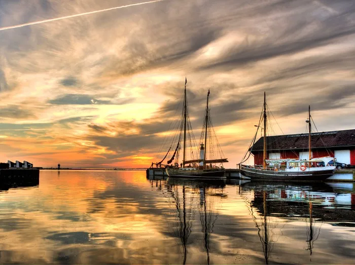 En seilbåt i Assens havn med solnedgang i bakgrunnen. Lei et feriehus i Assens for din neste ferie
