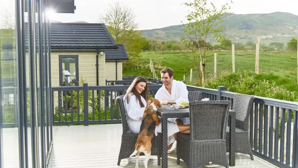 A couple and a dog outside their lodge at Keswick Lodge Retreat (KESW) in Keswick, Cumbria, The Lake District, England, UK