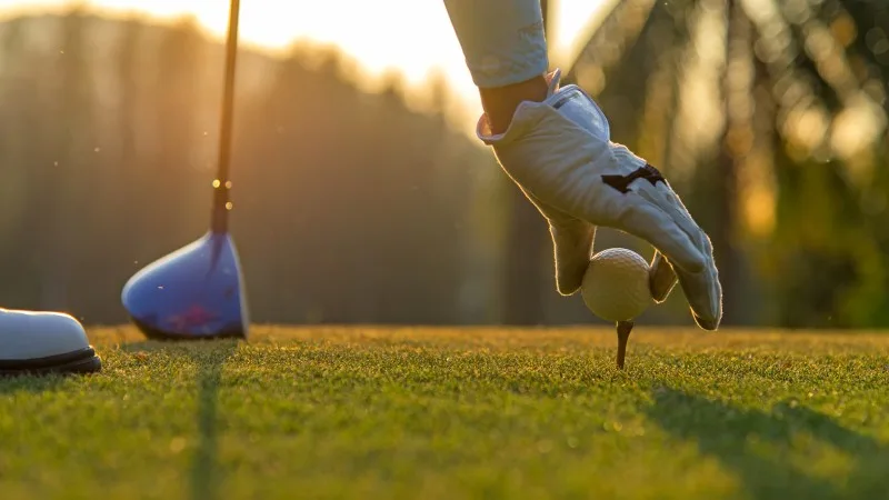 Hand asian woman putting golf ball on tee with club in golf course on evening and sunset time a for healthy sport.