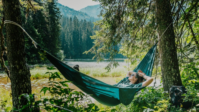 Young female hiker relaxing in a hammock by a crystal clear mountain lake.