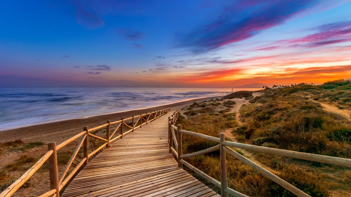 View of amazing bright sundown sky over waving sea and wooden path in countryside in Cabopino, Artola dunes. Marbella, Spain