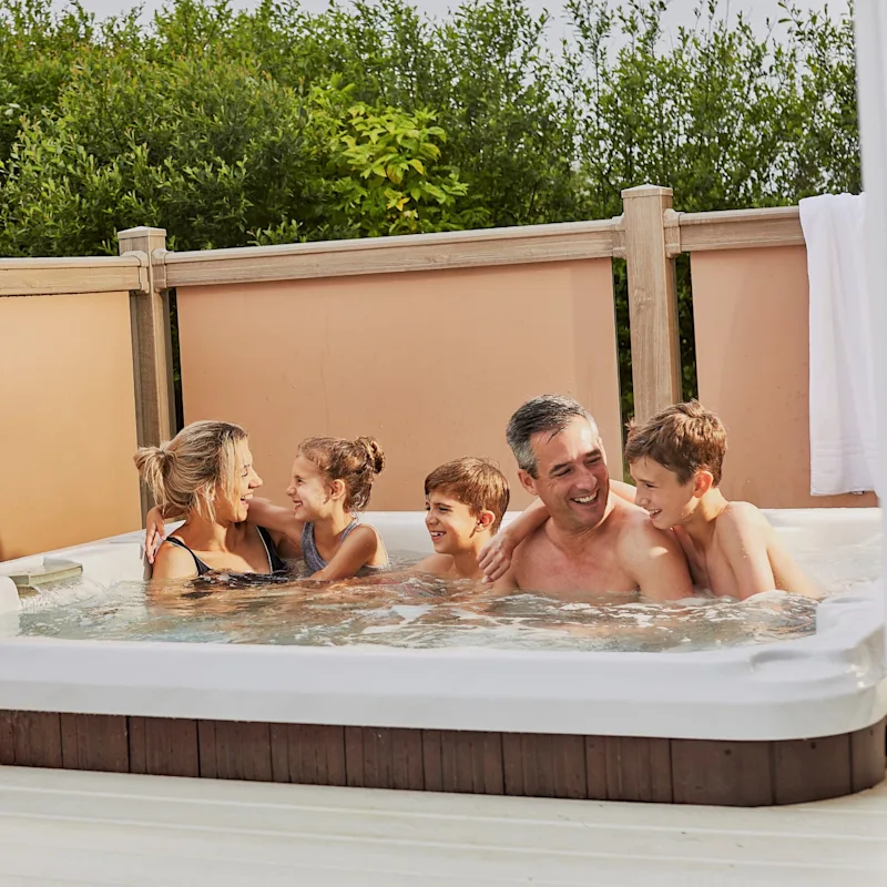 Family having fun in a private hot tub at their holiday lodge at Piran Meadows Resort in Cornwall, UK